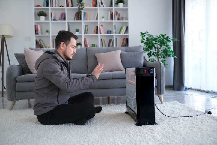 Man using a space heater to warm up his living room